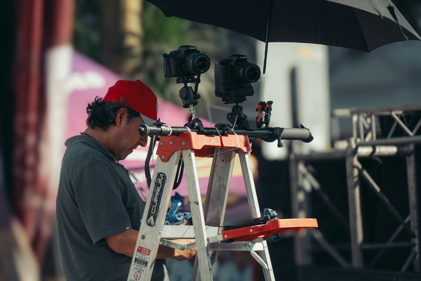 Man in red hat adjusts camera equipment on ladder