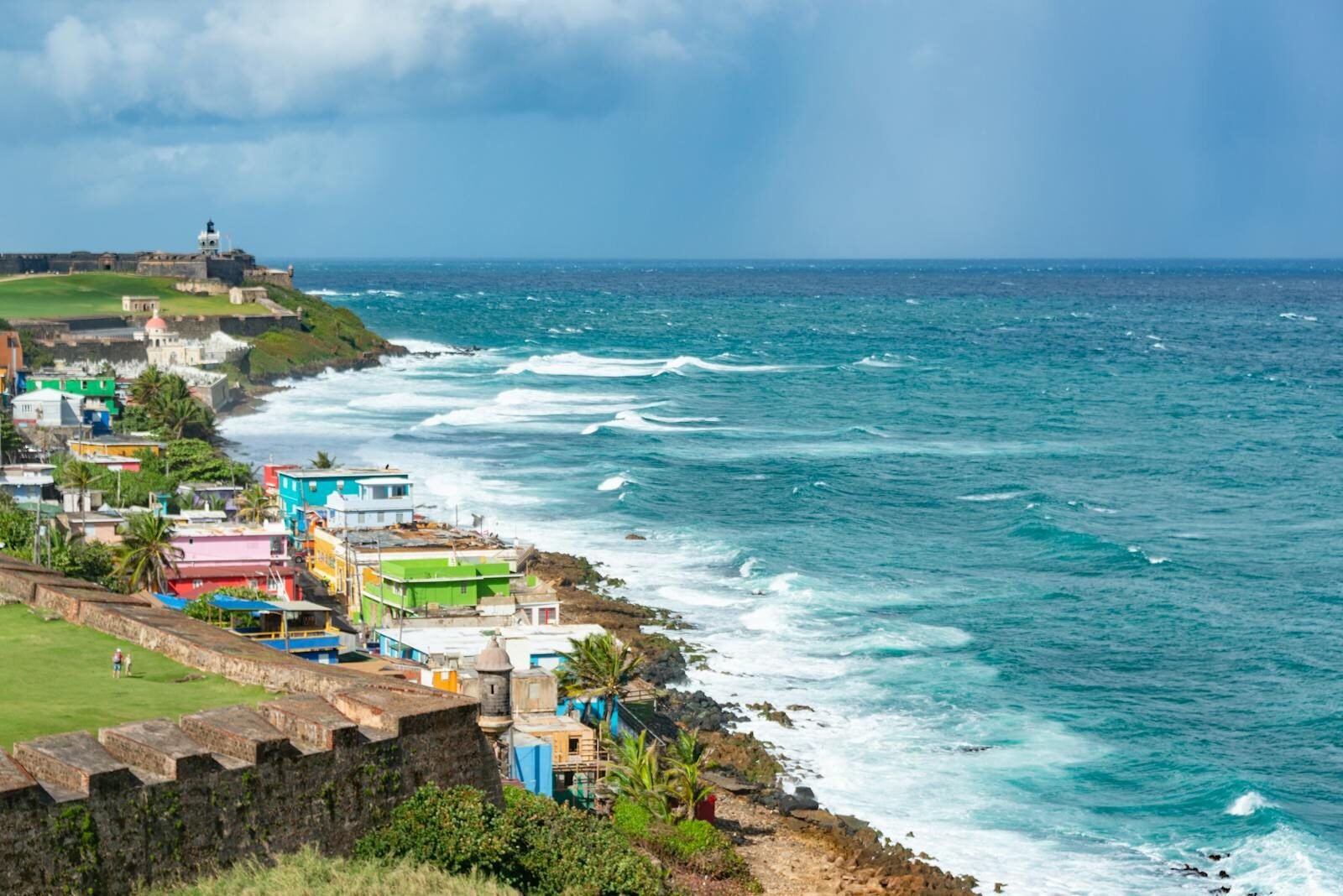 Colorful town along San Juan's coastline with waves crashing against the shore under a moody sky.