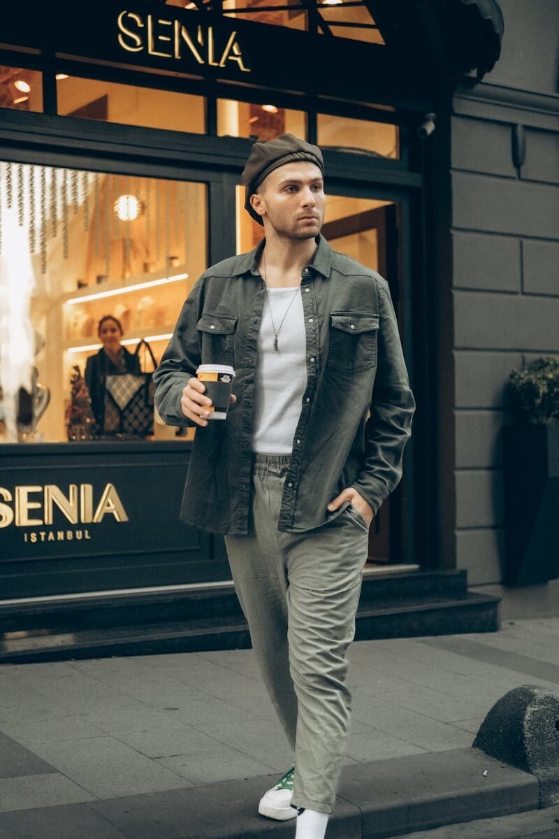 Stylish man wearing casual attire, holding coffee outside a fashion store in Istanbul.