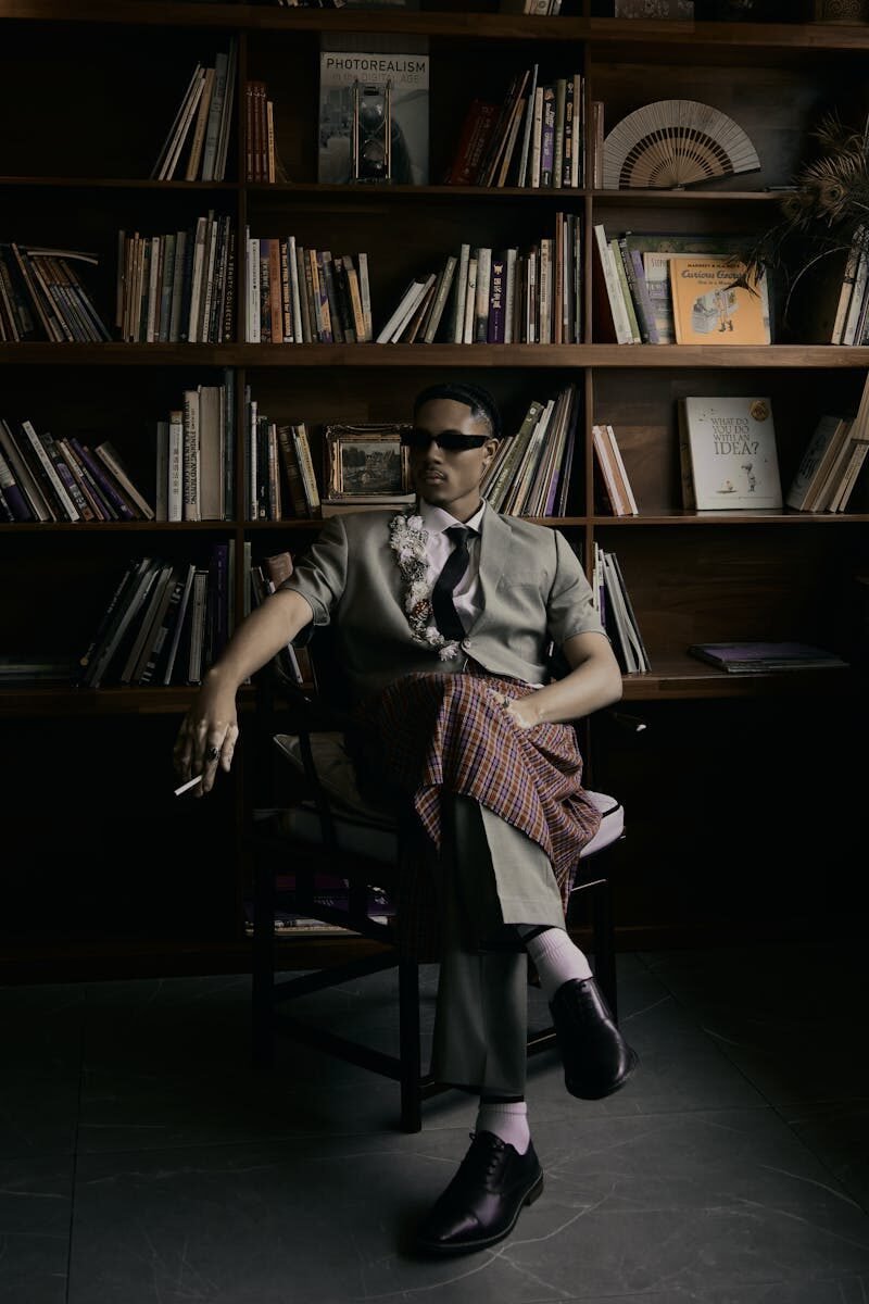 Sophisticated man seated with a cigarette in a stylish library setting.