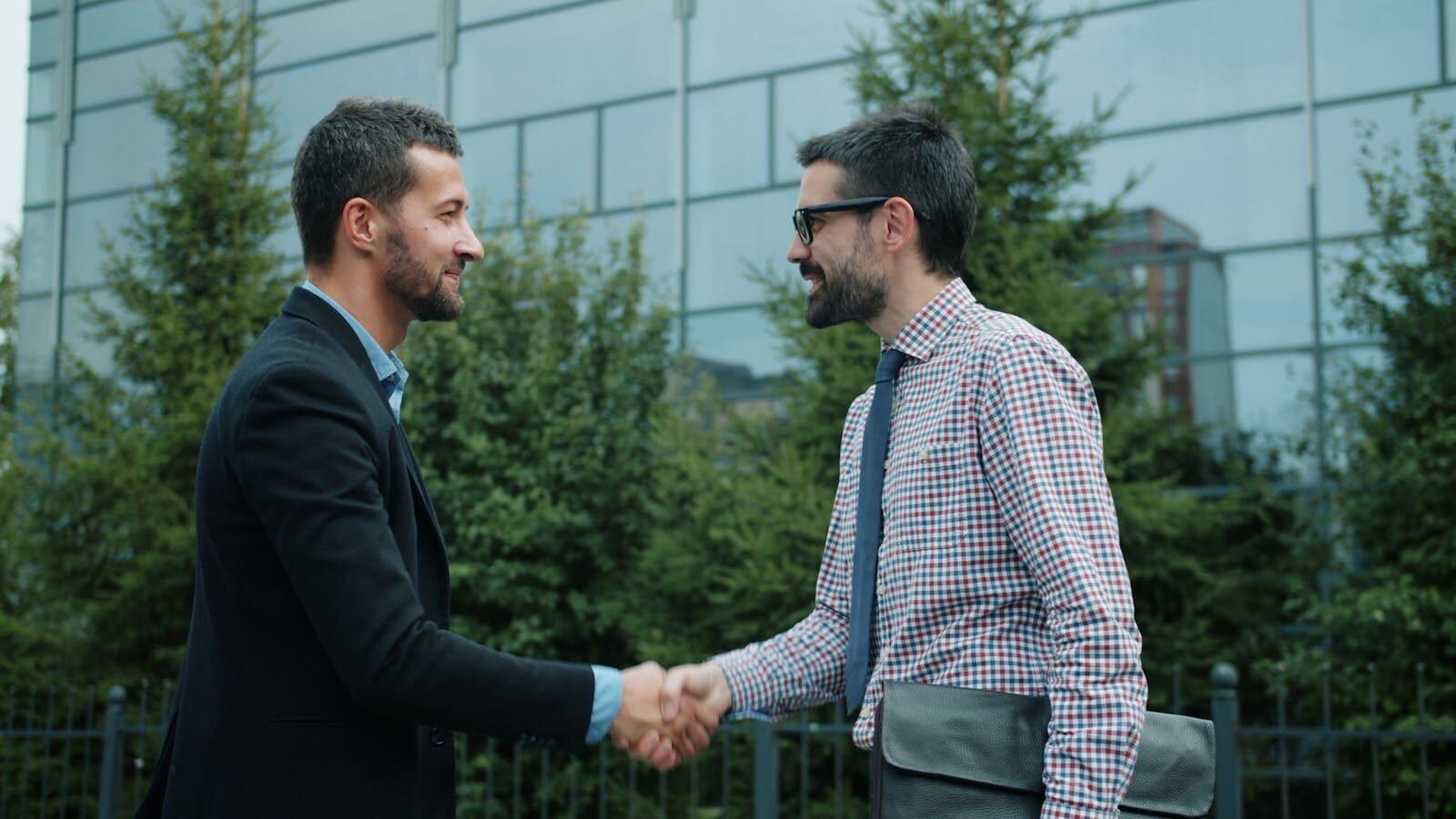 Two men shaking hands outside a modern office building, symbolizing business partnership.