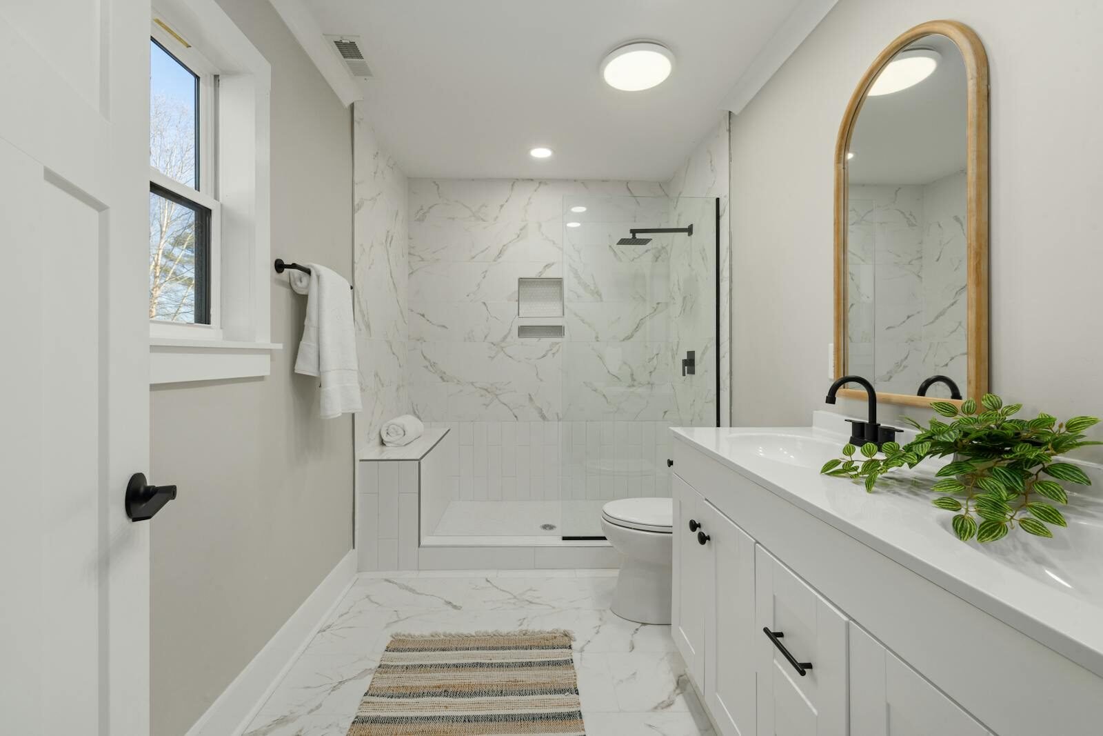 Bright modern bathroom featuring marble shower, large mirror, and sleek faucets.