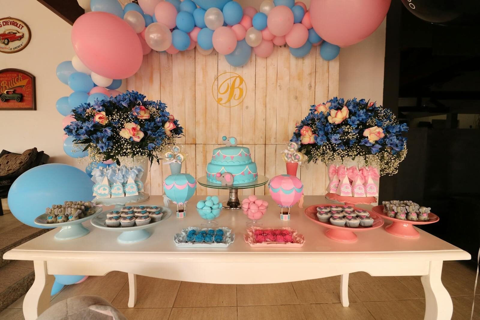 Vibrant dessert table decorated with blue and pink balloons, flowers, and sweets for a baby shower.